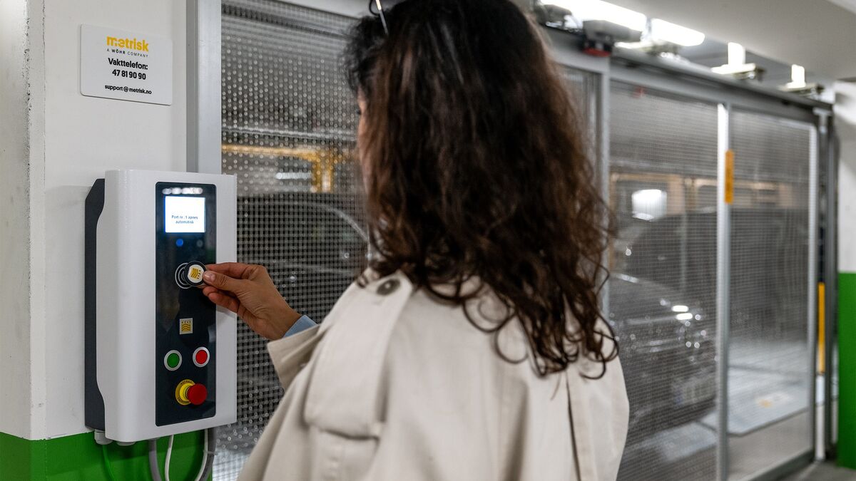 Une personne utilise le panneau de commande d’un système de stationnement semi-automatique pour récupérer un véhicule stationné. À l’arrière-plan, les emplacements de stationnement mobiles et un véhicule à l’intérieur de l’installation de stationnement so