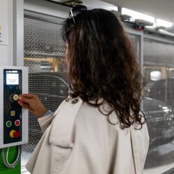 Une personne utilise le panneau de commande d’un système de stationnement semi-automatique pour récupérer un véhicule stationné. À l’arrière-plan, les emplacements de stationnement mobiles et un véhicule à l’intérieur de l’installation de stationnement so