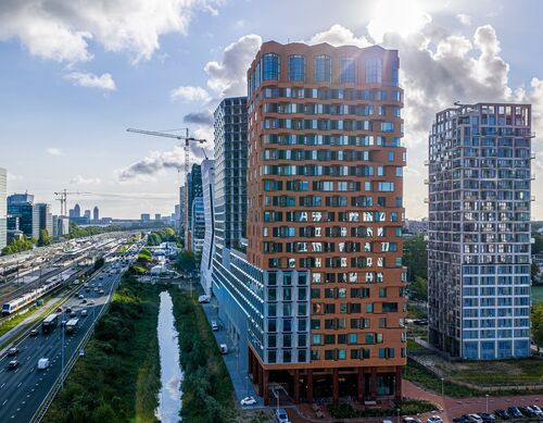 Vue extérieure du projet The Pulse à Amsterdam avec des immeubles de grande hauteur modernes et des infrastructures de transport urbain.