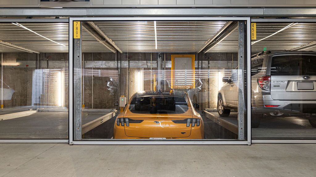 De afbeelding toont een gele sportwagen in een parkeersysteem binnen een moderne ondergrondse parkeergarage.