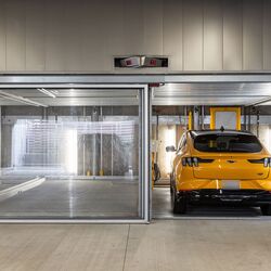 De afbeelding toont meerdere voertuigen in glazen parkeerplaatsen van een parkeersysteem in een moderne ondergrondse parkeergarage.