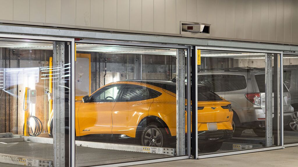 De afbeelding toont meerdere voertuigen in glazen parkeerplaatsen van een parkeersysteem in een moderne ondergrondse parkeergarage.