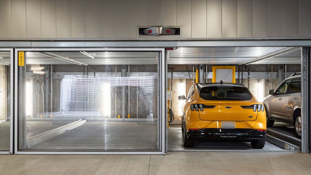 De afbeelding toont meerdere voertuigen in glazen parkeerplaatsen van een parkeersysteem in een moderne ondergrondse parkeergarage.