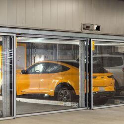 De afbeelding toont meerdere voertuigen in glazen parkeerplaatsen van een parkeersysteem in een moderne ondergrondse parkeergarage.